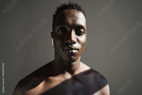 Close up portrait of a handsome fit muscular shirtless sportsman standing isolated over background, using wireless earphones