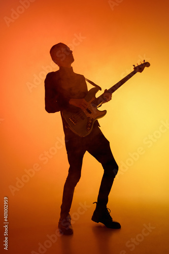 Smoke wave. Silhouette of young male guitarist isolated on orange gradient studio background in neon light. Beautiful shadow in action, performing. Concept of human emotions, expression, ad, music