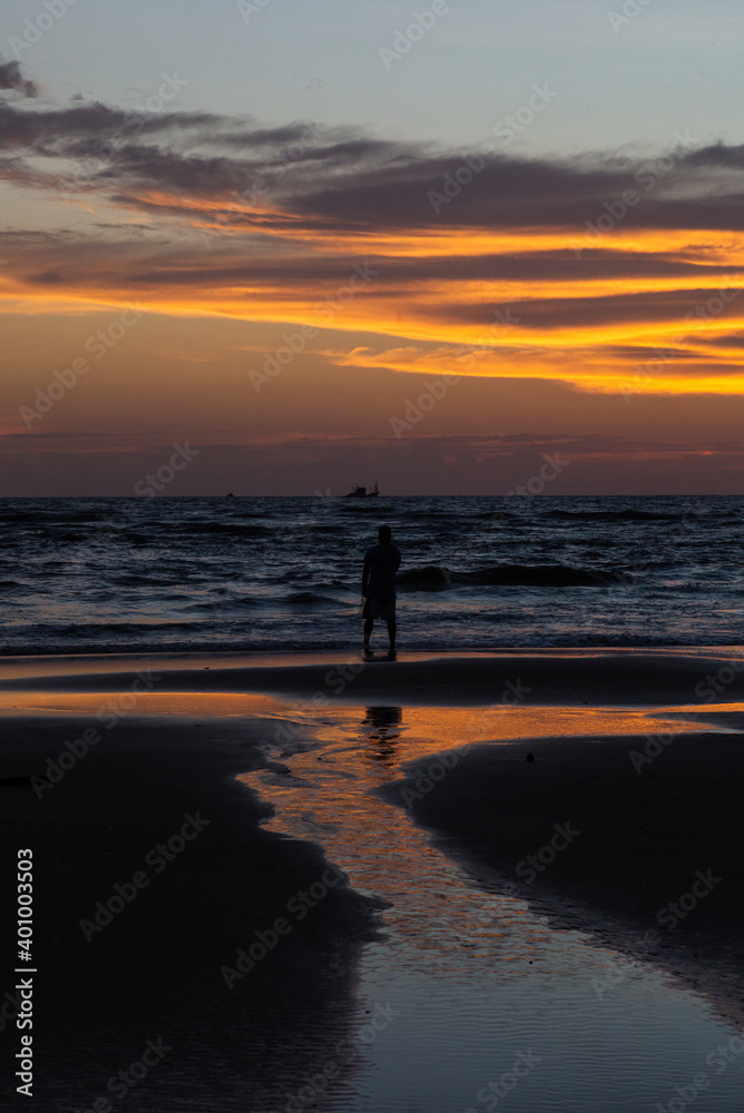 Silhouette of a man walking along the beach in sunset time