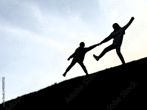 Silhouette of two people on top of the mountain. A loving couple stands against the background of the sky. The guy and the girl are holding hands.