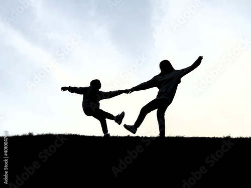 Silhouette of two people on top of the mountain. A loving couple stands against the background of the sky. The guy and the girl are holding hands.