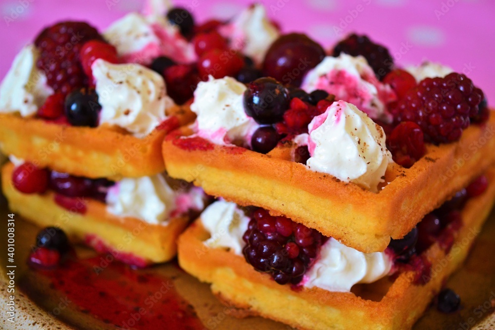 Close-up of a waffle filled with cream, cherries and berries on a pink cloth with white dots Close-up of a waffle filled with cream, cherries and berries on a pink cloth with white dots