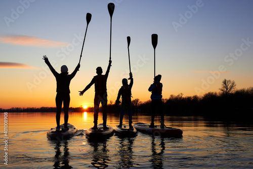 Four friends on stand up paddle board (SUP) on a flat quiet winter river at sunset raising his paddles up photo