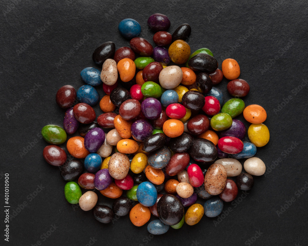 A heap of multi-colored glazed raisins on a black background. Rounded candies of different colors and sizes. Healthy and tasty snack. A heap of multi-colored glazed raisins on a black background. Rounded candies of different colors and sizes. Healthy and tasty snack.