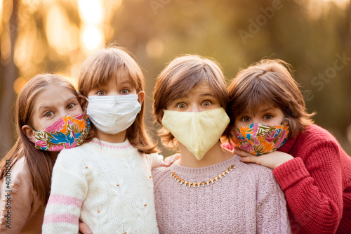 Group portrait of children in protective medical masks walking on street on sunset