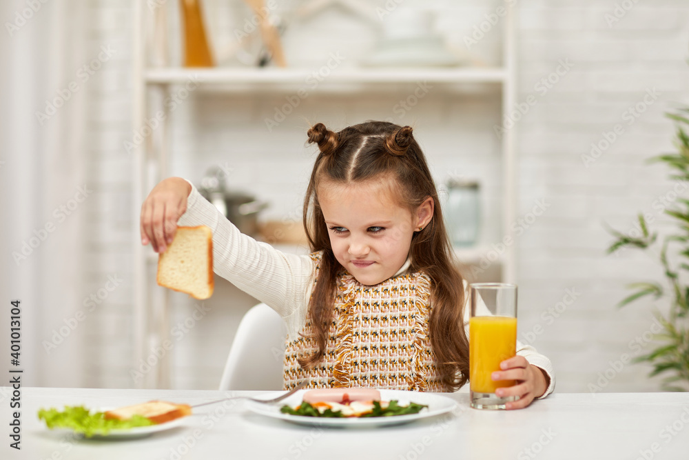 the child does not want to have breakfast. little girl looks at the sandwich with disgust