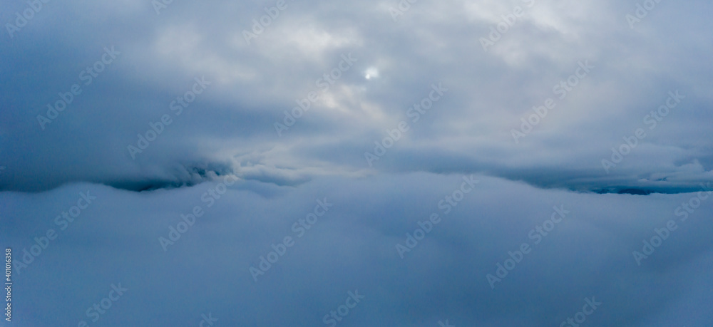 under cloudy sky and over cloud cover with mountain peak horizon and small sun point