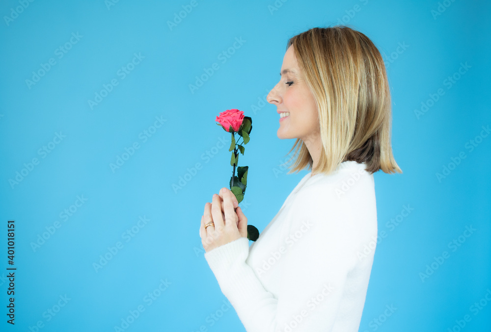 Profile portrait of young woman holding a flower over blue background. Profile portrait of young woman holding a flower over blue background.