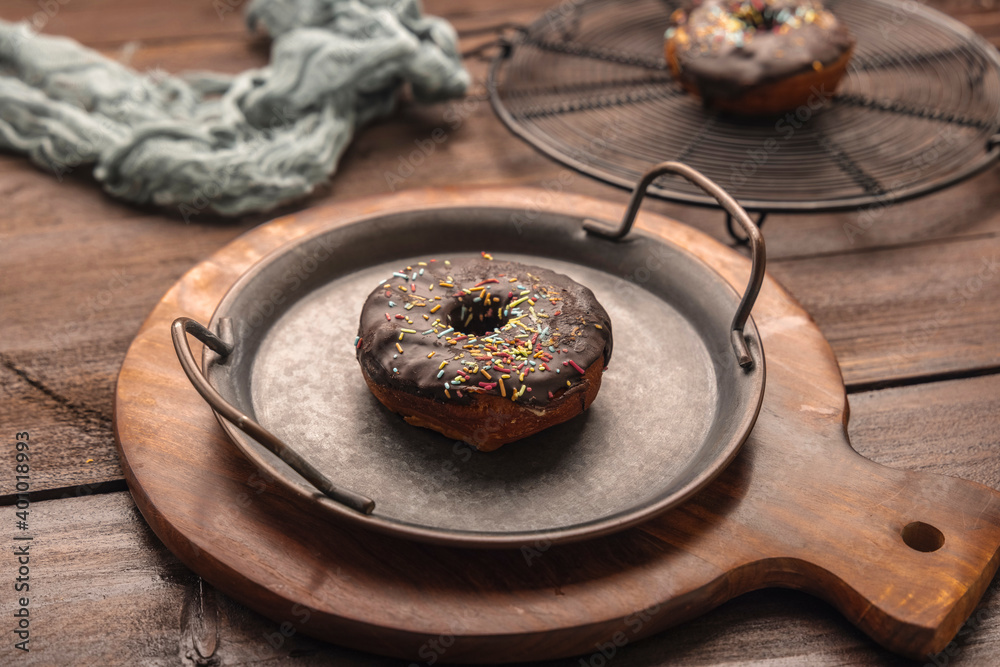 Chocolate frosted donut with colorful festive sprinkles kept in rustic iron plate Chocolate frosted donut with colorful festive sprinkles kept in rustic iron plate