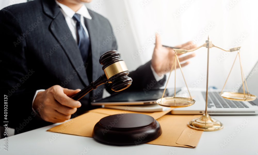 Justice and law concept.Male judge in a courtroom with the gavel, working with, computer and docking keyboard, eyeglasses, on table in morning light Justice and law concept.Male judge in a courtroom with the gavel, working with, computer and docking keyboard, eyeglasses, on table in morning light