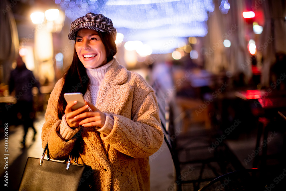 Pretty young woman using her mobile phone in the street at Christmas time Pretty young woman using her mobile phone in the street at Christmas time