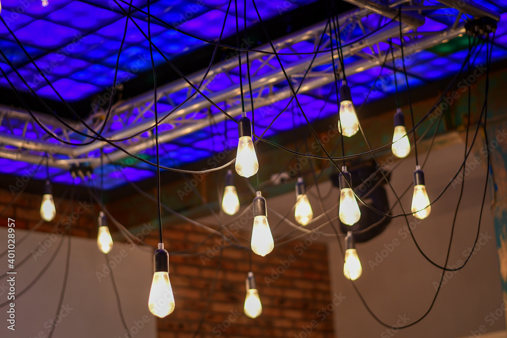 Decorative retro light bulbs hanging from the multicolored shining ceiling. Selective focus. 