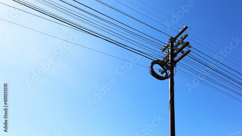 Roll the cables on a steel pole. Excessive wires are coiled in multiple loops on a metal pole. On a bright blue sky background with copy space. Selective focus