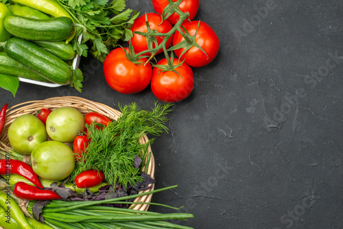 Above view of two vegetable baskets with a bunch of green and peppers cucumber and tomatoes with stem on dark background