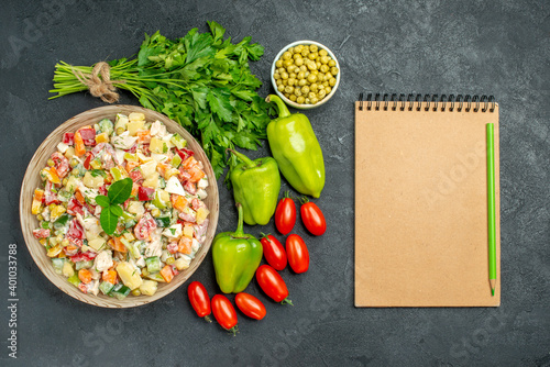 top view of bowl of vegetable salad with vegetables and notepad on side on dark green table