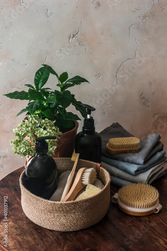 Bathroom interior still life. Natural bristle brush, shampoo bottle, towels, flower on dark background