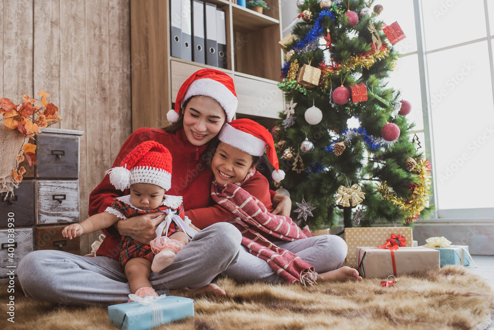 parent and two little children having fun and playing together near christmas tree indoors. merry christmas and happy holidays. cheerful mom and her cute daughters girls exchanging gifts.