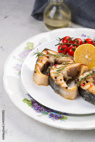 organic seafood. Grilled sturgeon steaks on a white plate with spices, cherry tomatoes and lemon. On a gray background.