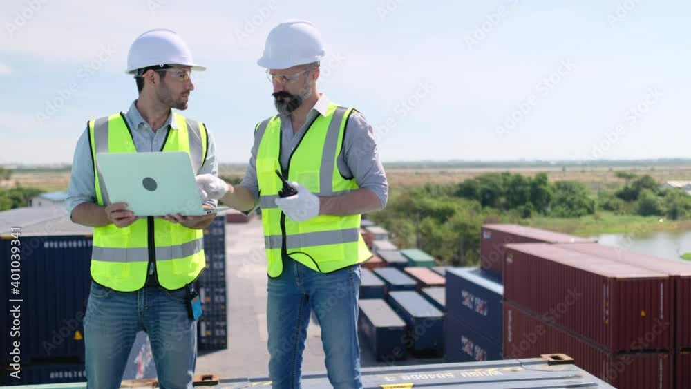 Engineer men or cargo container workers with safety uniform stay on high station and discuss together with work show in laptop. Concept of teamwork support management system factory industry. Engineer men or cargo container workers with safety uniform stay on high station and discuss together with work show in laptop. Concept of teamwork support management system factory industry.
