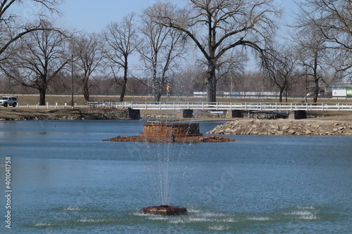 A long bridge over some water.Fountain and Bridge in Ta-Ha-Zouka Park Norfolk Nebraska March 2019