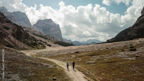 A couple hiking along a gravelled pathway leading through a valley in Italian Dolomites. High, sharp mountains around. Stony and raw landscape. Remote and desolate place. Freedom of exploration