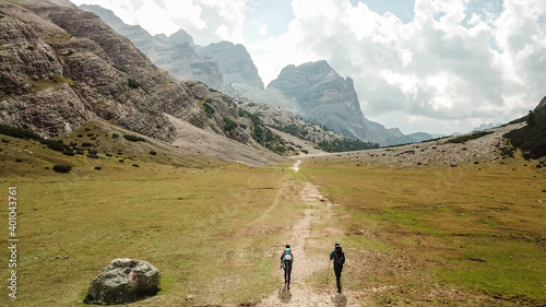 A couple hiking along a pathway leading through a valley in Italian Dolomites. High, sharp mountains around. Stony and raw landscape, green meadow. Remote and desolate place. Freedom of exploration photo