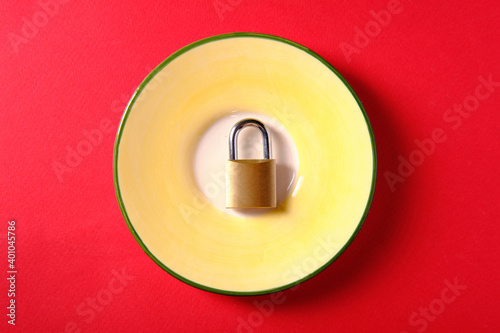Metal padlock on a plate, on a red background, a symbol of diet