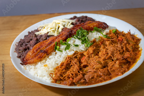 white plate with Venezuelan food, meat, fried plantain, rice, and beans