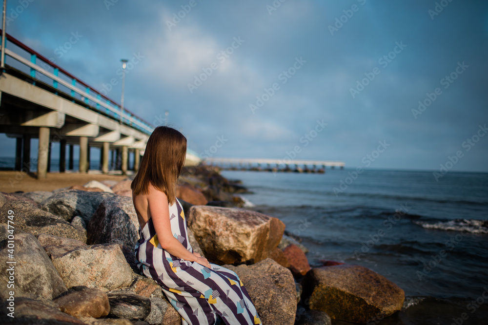 portrait of a girl who sits on stones at the pier near the sea