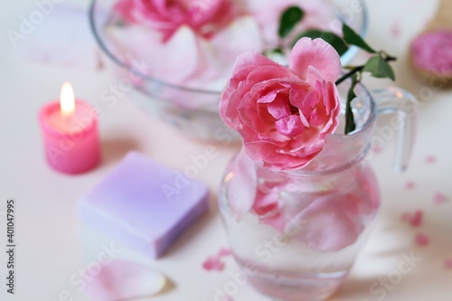 Fototapeta Naklejka Na Ścianę i Meble -  Fresh pink roses, water, petals, candles on a light background, body care products, natural home cosmetics, healthy lifestyle