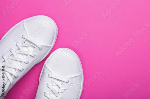 Pair of stylish sport shoes on pink background. Top view of white sneakers on color background with space for text 
