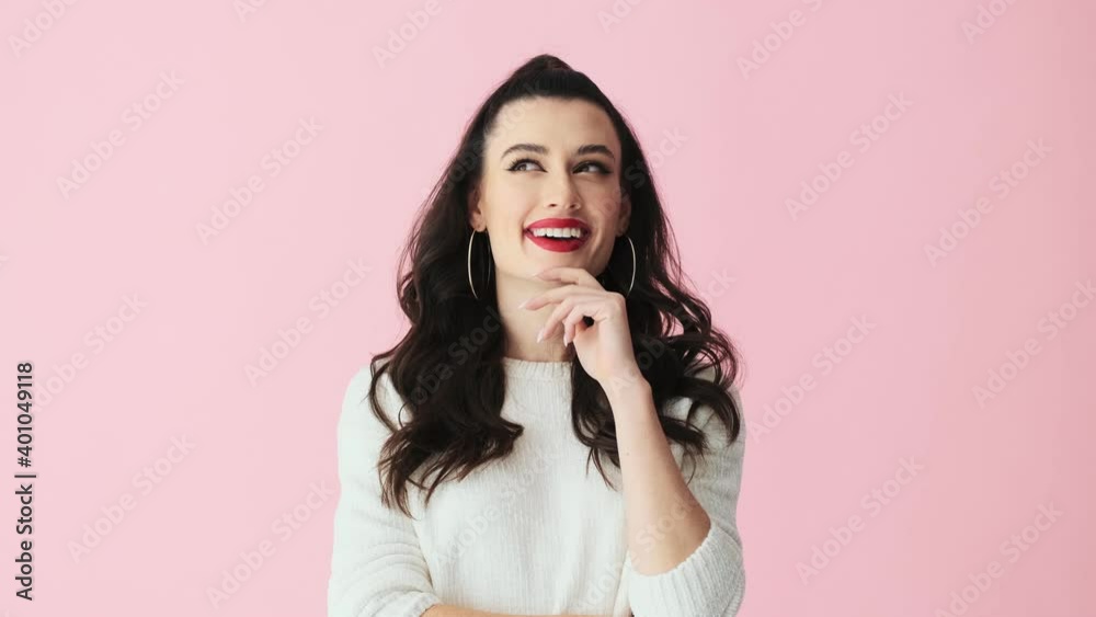 A dreaming woman with red lips is standing isolated over pink background in studio A dreaming woman with red lips is standing isolated over pink background in studio