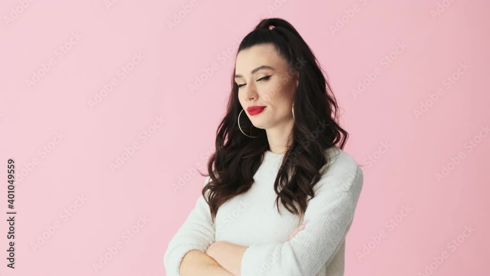 A displeased woman with red lips and crossed hands is feeling bored standing isolated over pink background in studio A displeased woman with red lips and crossed hands is feeling bored standing isolated over pink background in studio