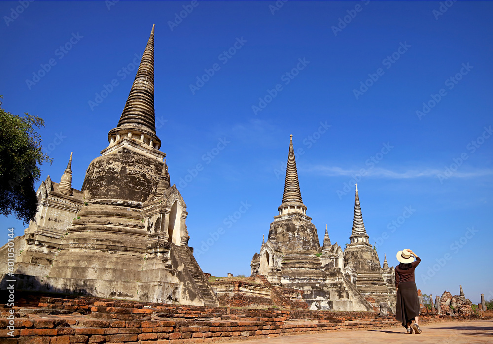 Fototapeta premium Female Visitor in White Hat Walking along the Incredible Historic Pagoda Ruins of Wat Phra Si Sanphet in Ayutthaya, Thailand