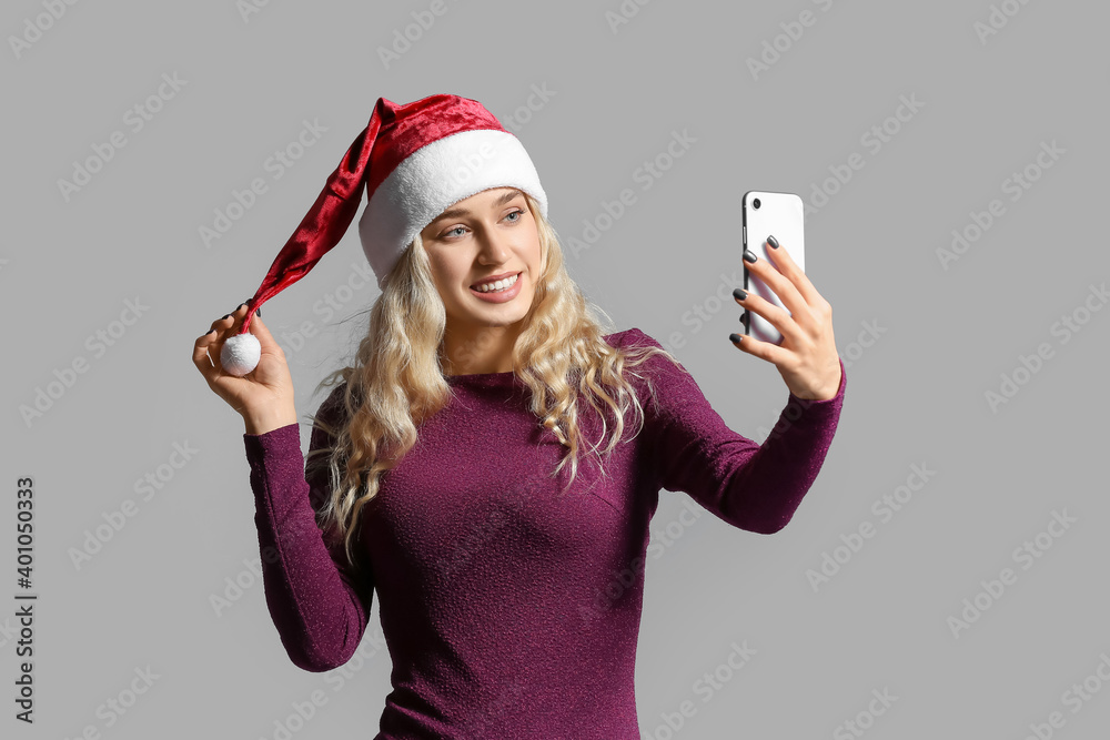 Beautiful young woman in Santa hat with mobile phone on light background Beautiful young woman in Santa hat with mobile phone on light background