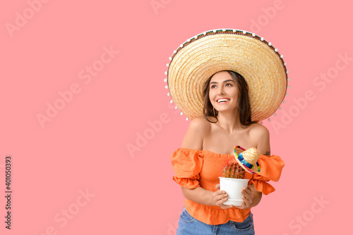 Beautiful young woman in sombrero hat and with cactus on color background photo