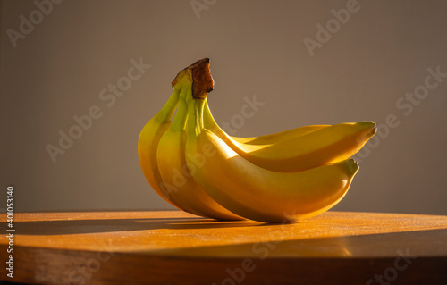 Still life of bananas. Bunch of bananas on a wooden table lit by natural sunlight. Minimal creative design. Dark background,