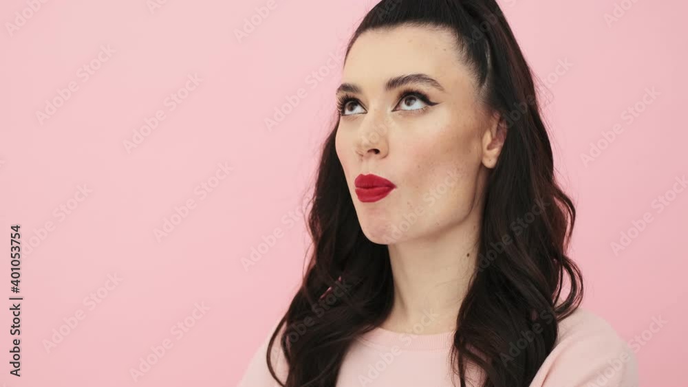 An attractive woman with red lips is eating bubblegum standing isolated over a pink background in the studio An attractive woman with red lips is eating bubblegum standing isolated over a pink background in the studio