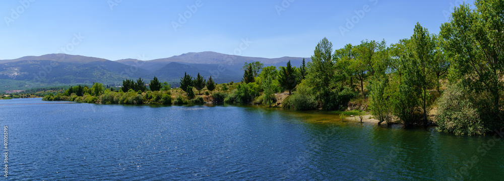 Panoramic lake landscape in the mountains with trees and green vegetation.
