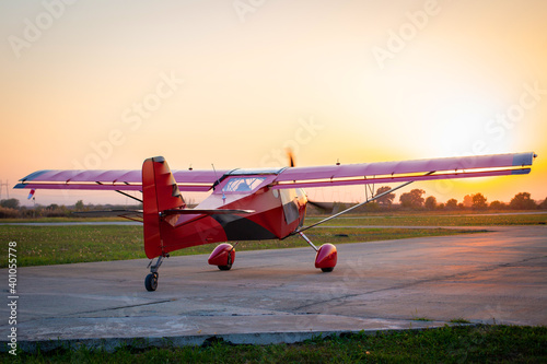 Small private lightweight propeller airplane against the sunset. Red aircraft on the runway.