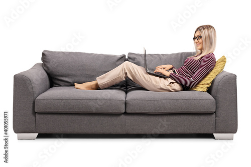 Young woman working on a laptop and laying on a sofa