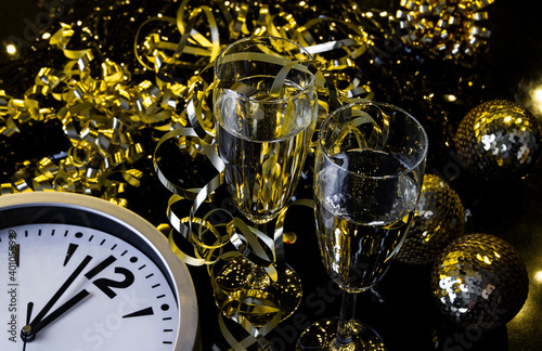 Two glasses of champagne, golden decorations and clock approaching midnight. New Year's Eve celebration composition.