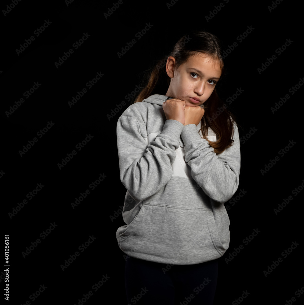 Beautiful little girl in gray sweatshirt and two pigtails posing in lovely pose on black background Beautiful little girl in gray sweatshirt and two pigtails posing in lovely pose on black background