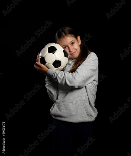 Little girl in gray sweatshirt and two pigtails playing with a soccer ball isolated on black background © Andres