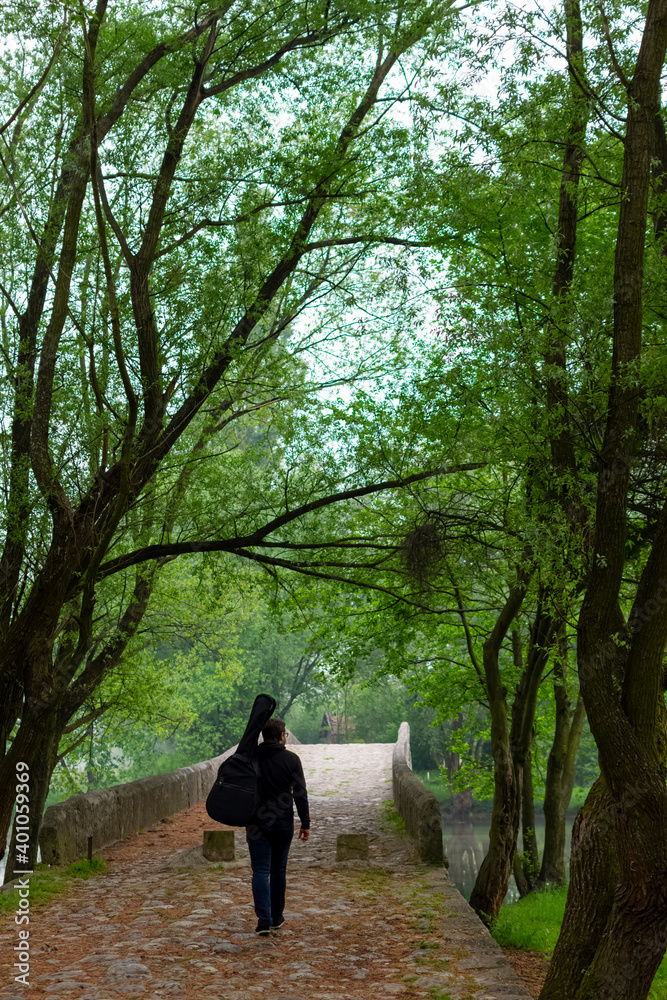 Young man carry guitar bag while walking alone through the forest. Enjoying in nature beauty Young man carry guitar bag while walking alone through the forest. Enjoying in nature beauty