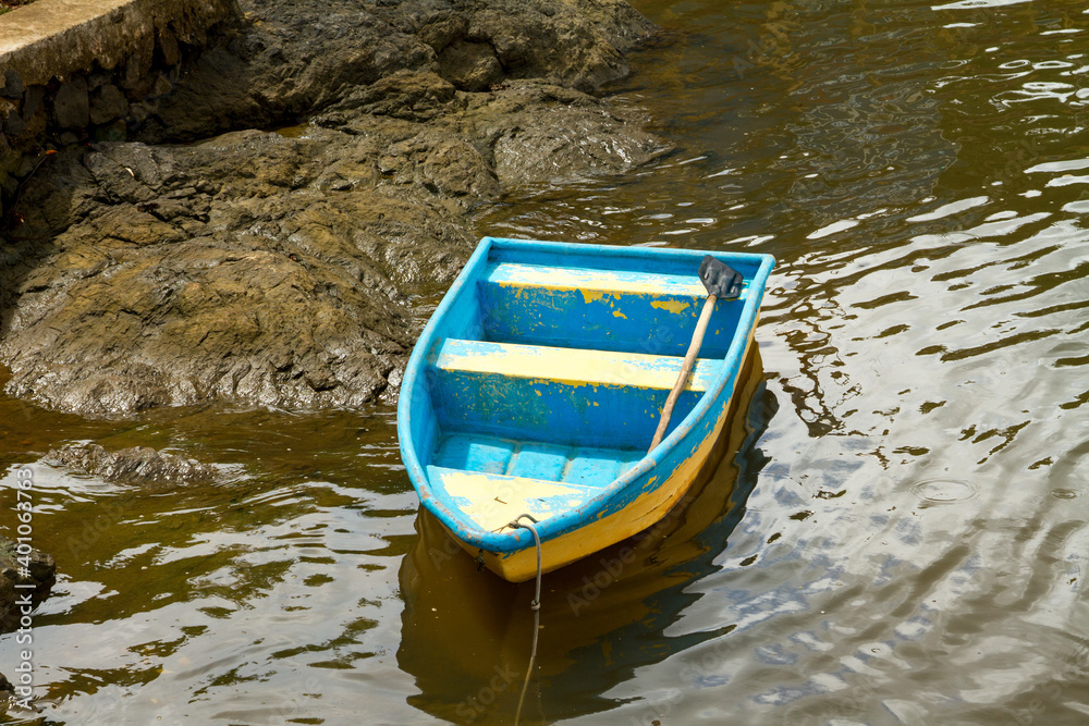 Little blue and yellow row boat sitting abandoned on the shore of a river Little blue and yellow row boat sitting abandoned on the shore of a river