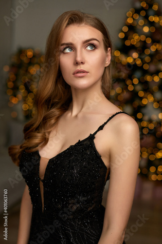 portrait of elegant woman in black evening dress over christmas tree