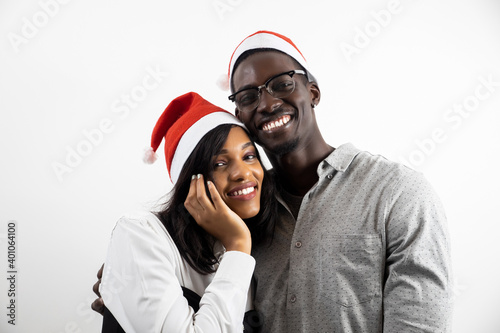 Portrait of a cheerful young African couple wearing Christmas hats, hugging, isolated on a light background © vitalii_demin