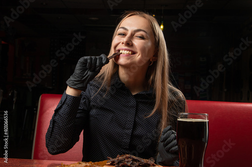 a satisfied girl is eating snacks  a model is holding a jerky in black gloves  a beer is on the table  dinner is in a pub.