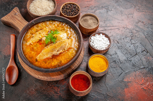 bottom view chicken soup in wooden bowl on chopping board wooden spoon black pepper red pepper turmeric sea salt rice on dark red background with free space